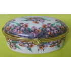 Декоративная фарфоровая шкатулка (или дринкет) овальной формы с цветочным узором, напоминающим орхидеи, и золотистой металлической фурнитурой.