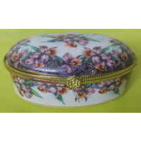 Декоративная фарфоровая шкатулка (или дринкет) овальной формы с цветочным узором, напоминающим орхидеи, и золотистой металлической фурнитурой.